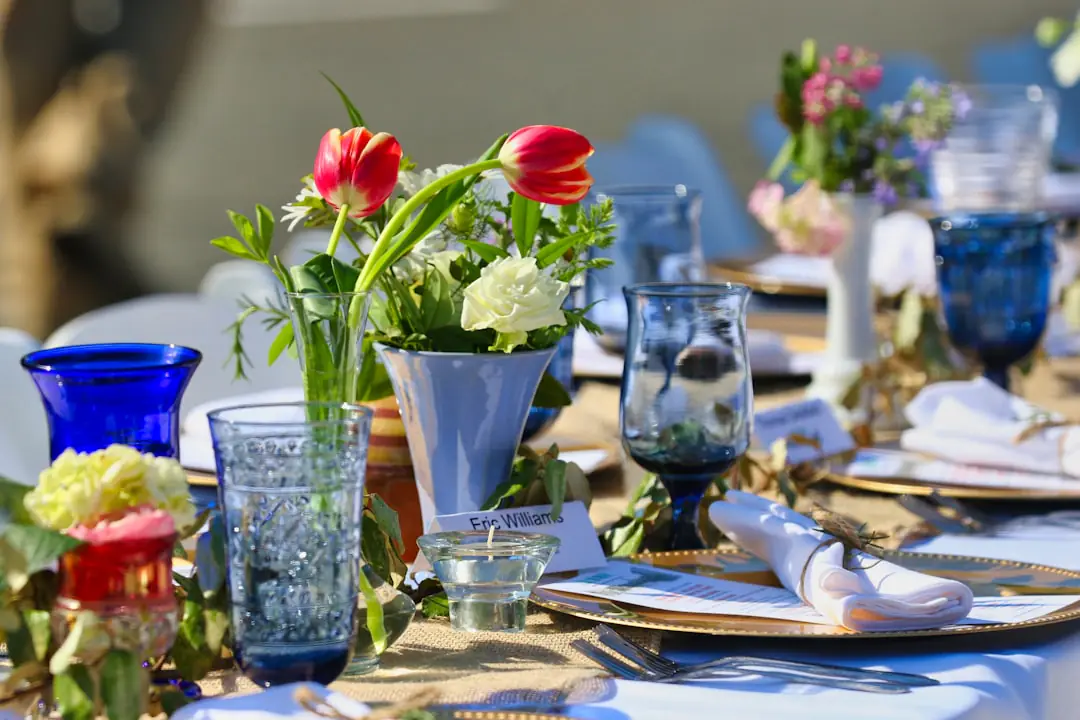 Chemin de table végétal avec fleurs roses, feuillages et aromatiques dans de petits vases sur une table d’été