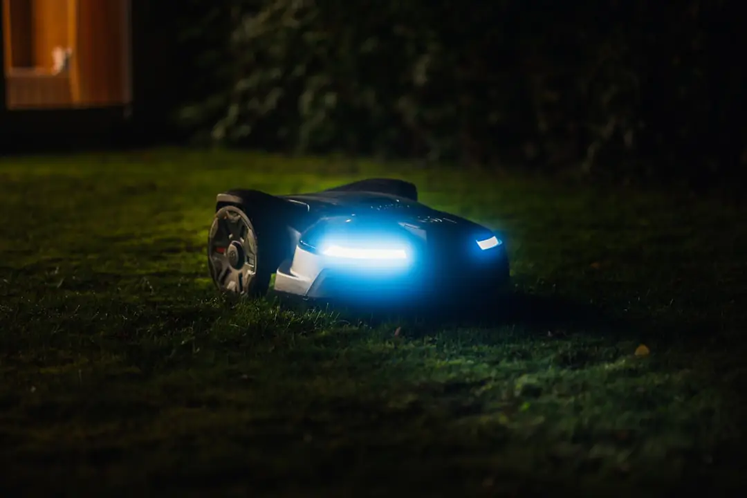 Robot tondeuse compact en fonctionnement sur une pelouse française bordée de massifs et de vivaces