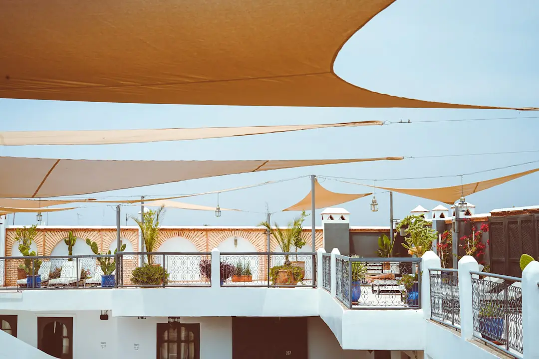 Terrasse en bois française ombragée par une voile écrue, une pergola végétalisée et de grands pots fleuris