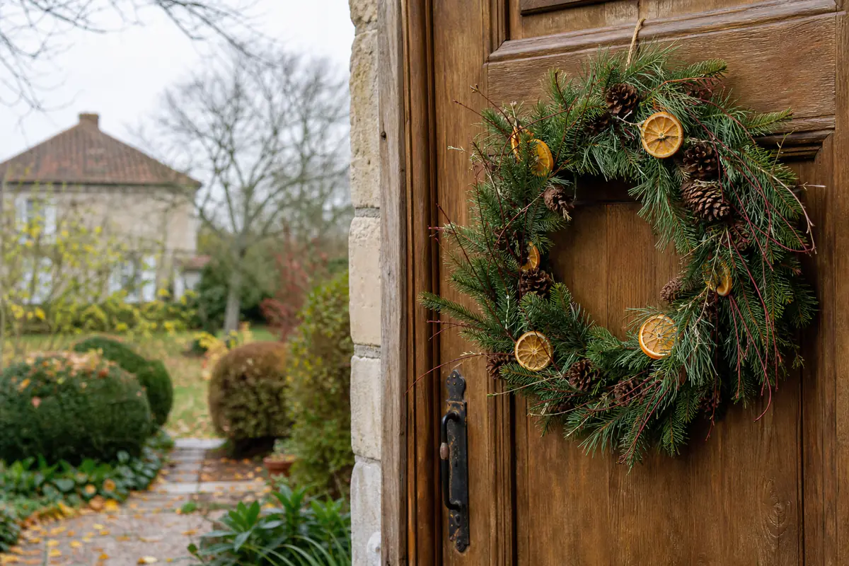Couronne de Noël naturelle en pin, oranges séchées et pommes de pin suspendue à une porte en bois