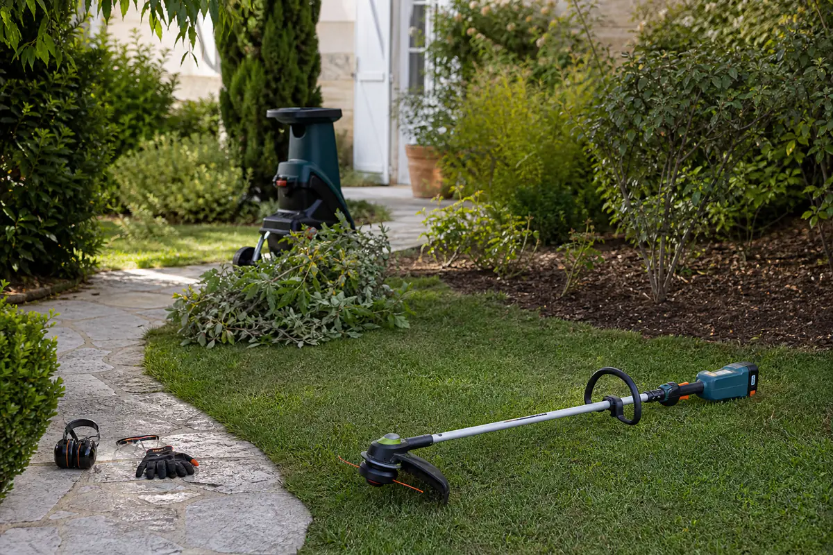 Débroussailleuse, coupe-bordure et branches prêtes à être broyées dans un jardin familial soigné