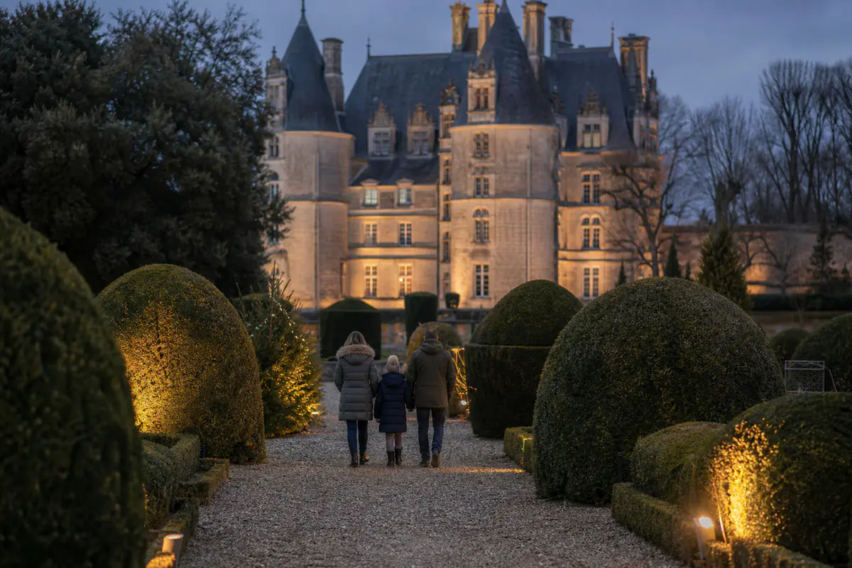 Allée illuminée d’un château français entourée de haies taillées et de grands arbres dans un jardin d’hiver