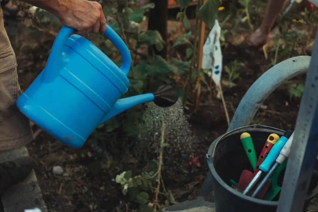 Cinq outils de jardinage modernes posés sur une pelouse près d’un potager prêt pour le printemps