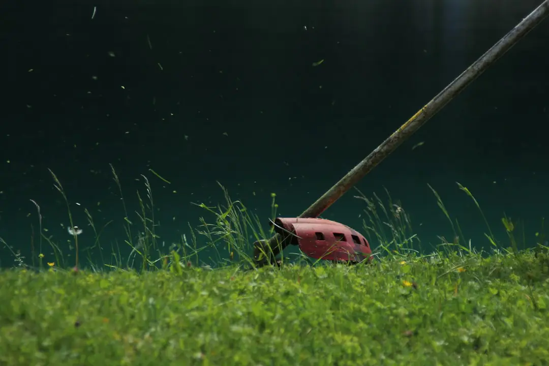 Jardinier équipé d’un casque utilisant une débroussailleuse thermique multifonction dans un jardin français arboré