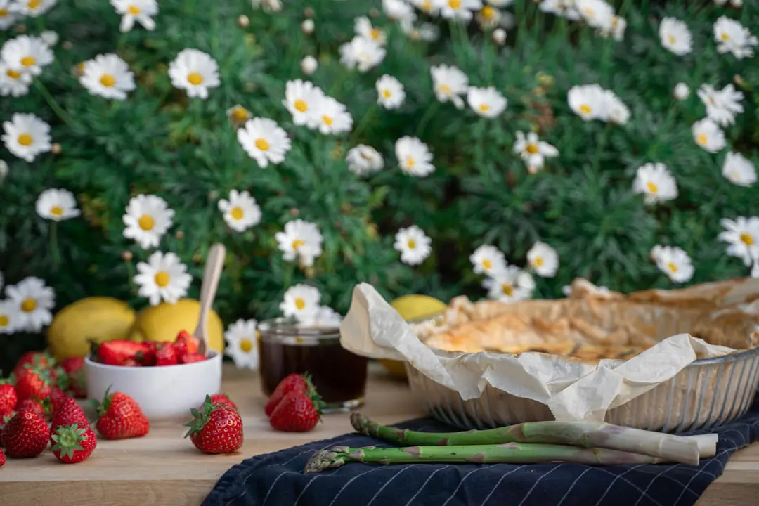 Jeune fraisier en fleur au potager, main retirant un bouton, paille au sol et autres fleurs blanches intactes