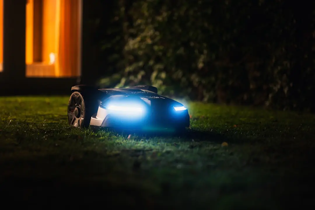 Robot tondeuse compact en fonctionnement sur une petite pelouse française bordée de massifs et d’arbustes