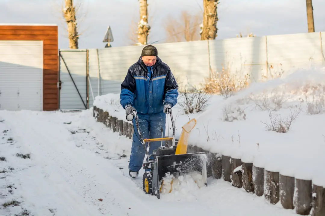 Jardin familial français en hiver, massifs couverts de feuilles et jardinier nettoyant ses outils près d’un arbuste
