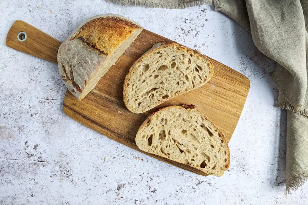 Miche de pain au levain aux herbes fraîches posée sur une table de jardin près d’un potager aromatique