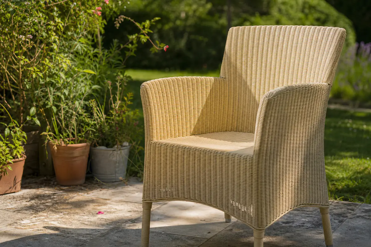Fauteuil de jardin en résine tressée blanche légèrement jaunie exposé au soleil sur une terrasse française