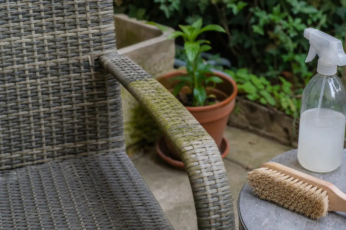 Chaise de jardin en résine tressée avec un film d'algues vertes sur l'accoudoir, brosse et vinaigre blanc à proximité