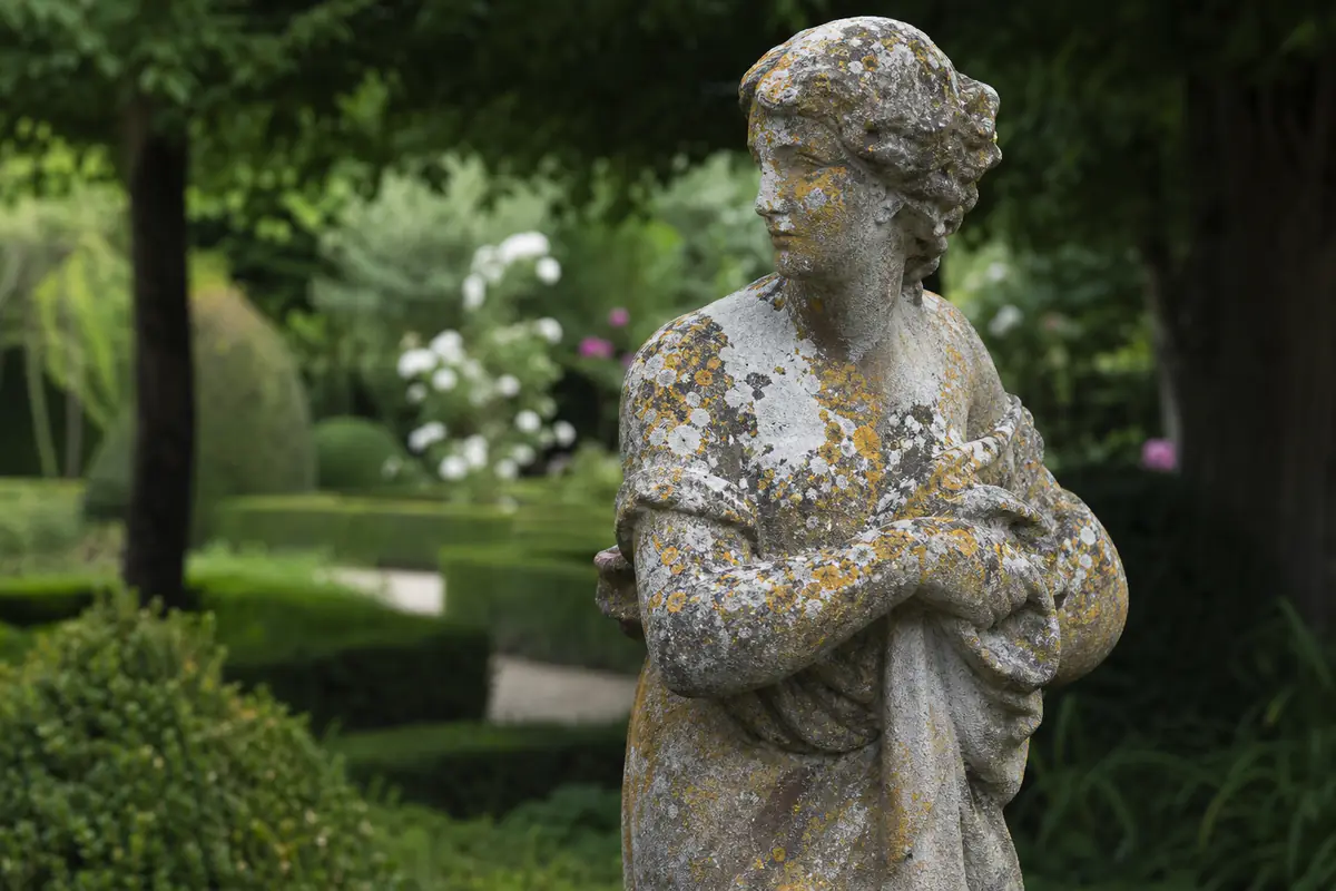 Statue de jardin en pierre partiellement recouverte de lichen grisâtre dans un jardin français ombragé