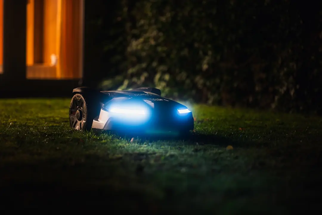 Robot tondeuse compact en fonctionnement sur une pelouse verte bordée de massifs dans un jardin français