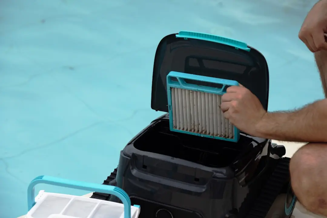 Petit robot de nettoyage au fond d’une piscine hors-sol, eau claire et jardin français ensoleillé autour