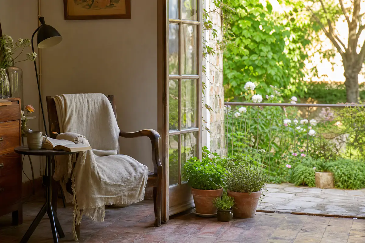 Fauteuil de lecture en bois près d’une baie vitrée, face à des pots d’aromatiques et un petit jardin verdoyant