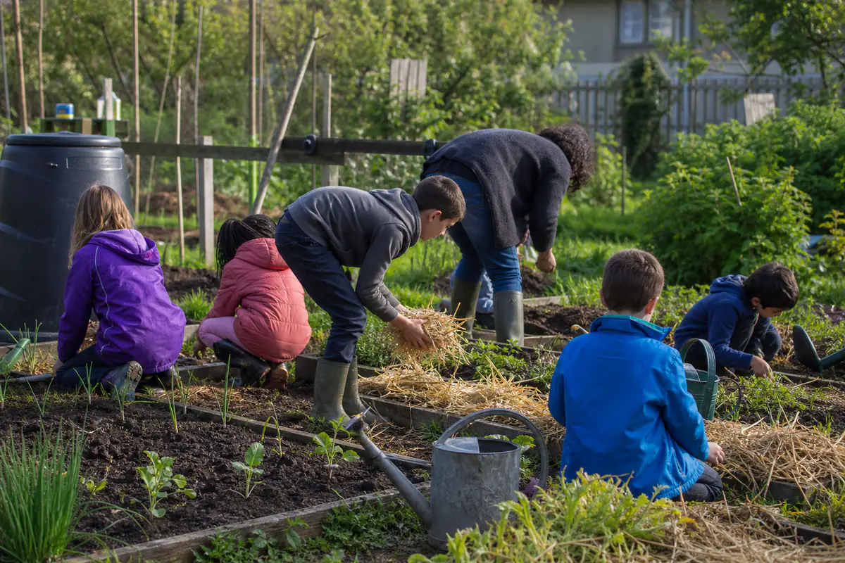 Groupe d’enfants préparant des semis et paillant des bacs potagers avec un adulte dans un jardin partagé