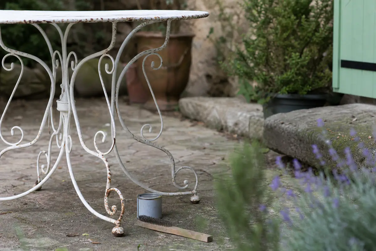 Table de jardin en fer forgé avec des points de rouille visibles sur un pied, brosse métallique posée à côté