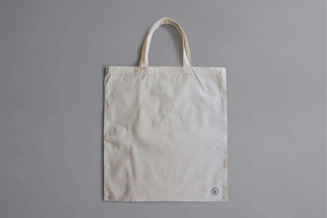 Sac fourre-tout beige à poches posé sur un banc de jardin, avec gants, carnet, sécateur fermé et livres