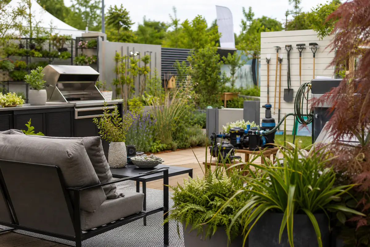 Visiteurs observant un barbecue et du mobilier durable dans un espace de jardin lumineux et végétalisé