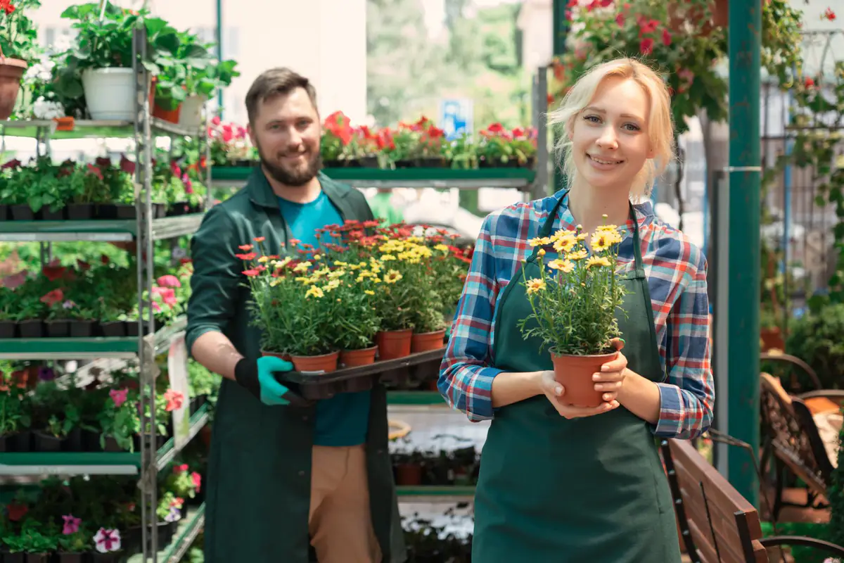 Jardinier portant un tablier de jardinage en toile, réglant ses poches près d’un potager familial