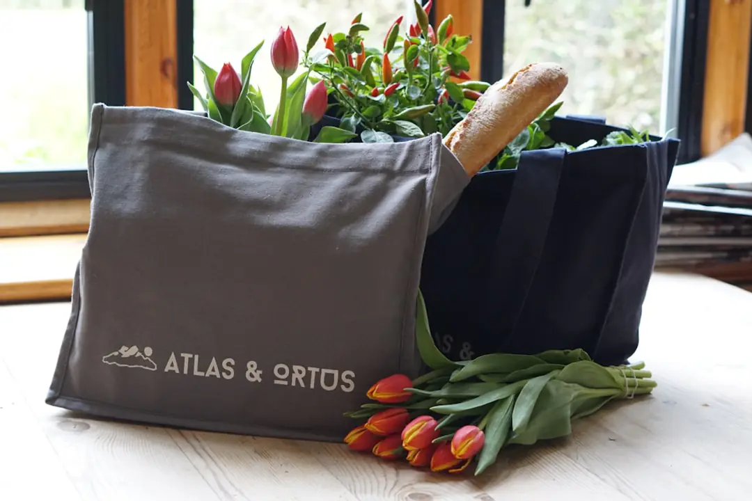 Sac de jardinage personnalisé en toile posé sur une table de rempotage dans un jardin français fleuri