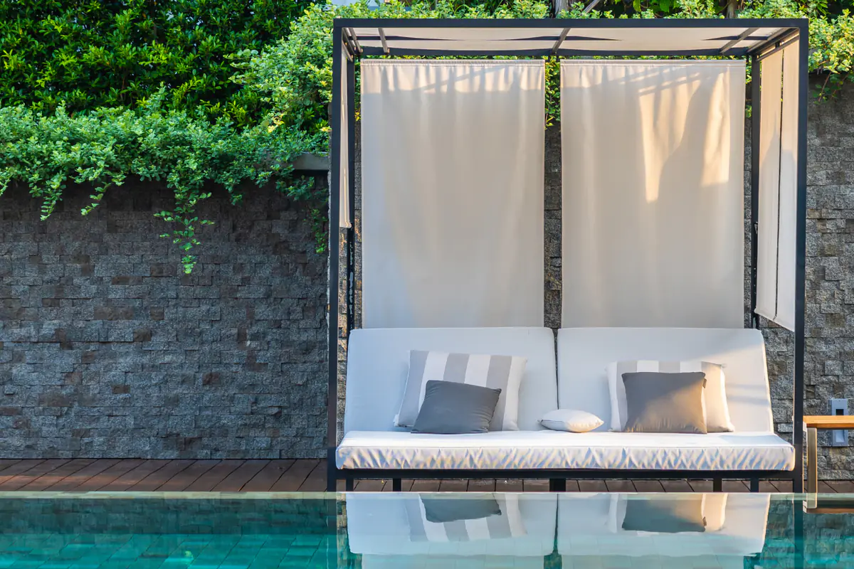 Pergola en bois dans un jardin français avec voilages écrus noués aux poteaux et salon de terrasse ombragé
