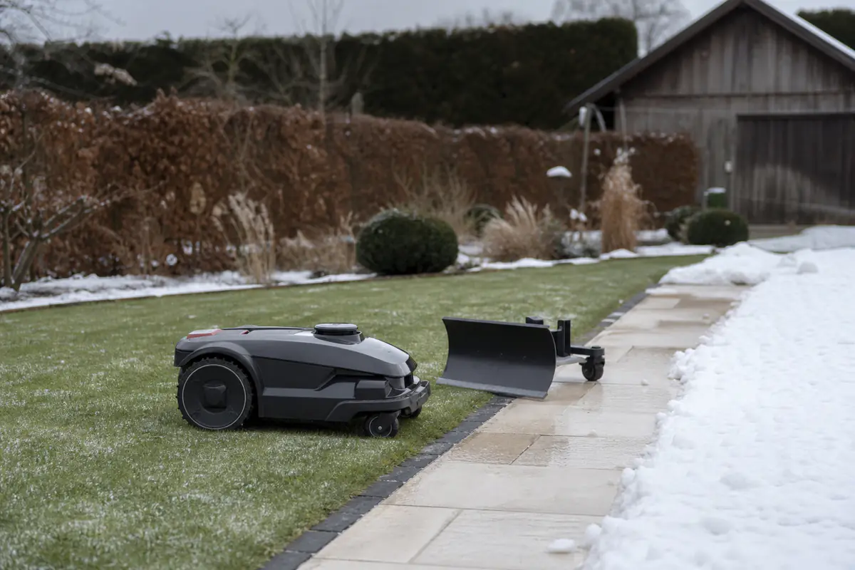 Robot de jardin multifonction circulant sur une pelouse près d’une allée enneigée dans un jardin français